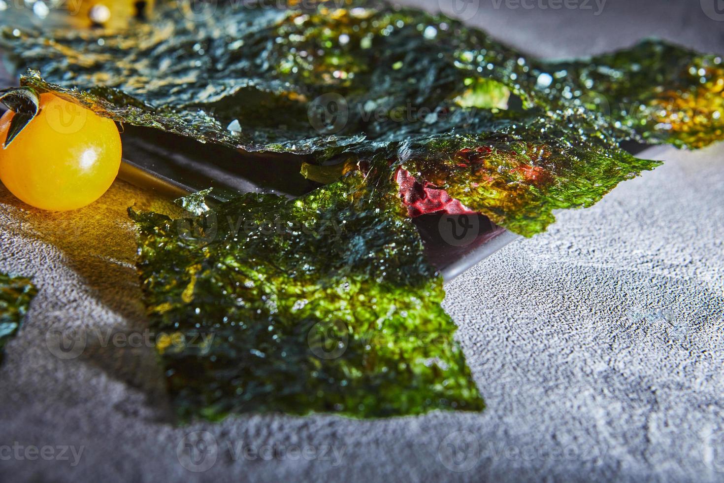 Alga nori crujiente con tomates cherry y especias oscuras sobre hormigón gris foto