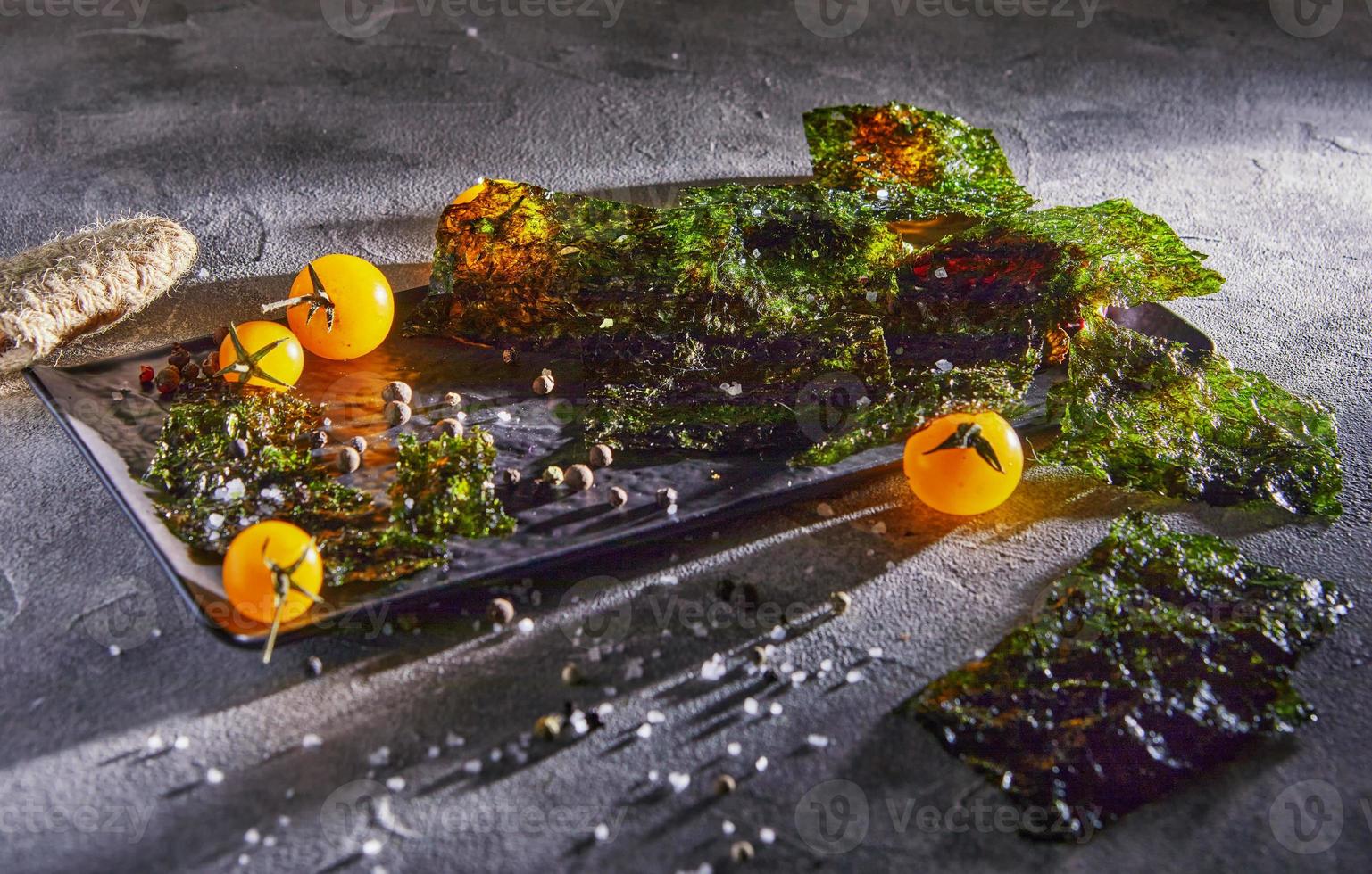 Alga nori crujiente con tomates cherry y especias oscuras sobre hormigón gris foto