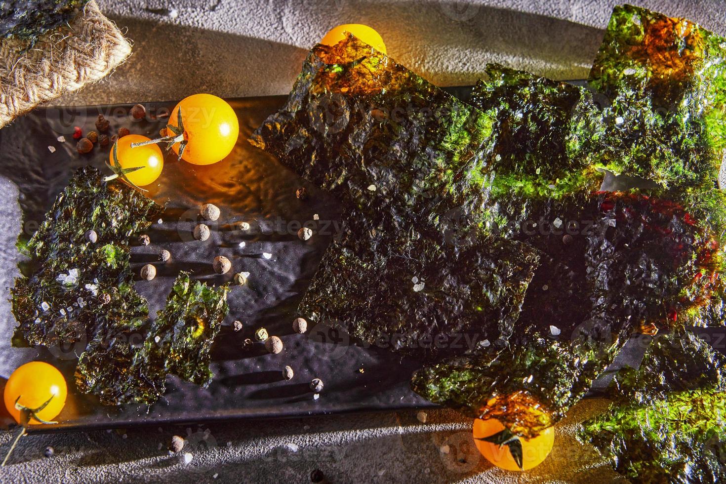 Crispy nori seaweed with cherry tomatoes and dark spices on gray concrete photo