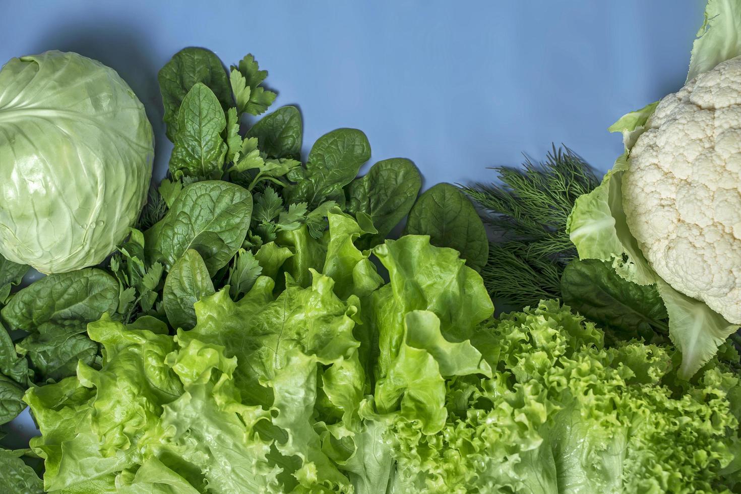 Dieta vegetariana verde de repollo, coliflor, lechuga y espinacas sobre un fondo azul. foto