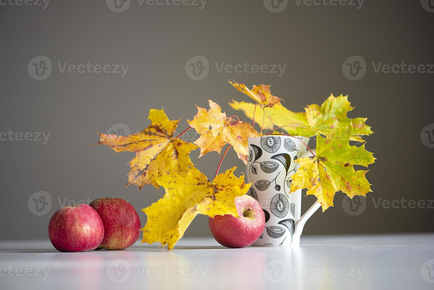 Autumn still life with red apples and colorful maple leaves in a cup on a gray background photo