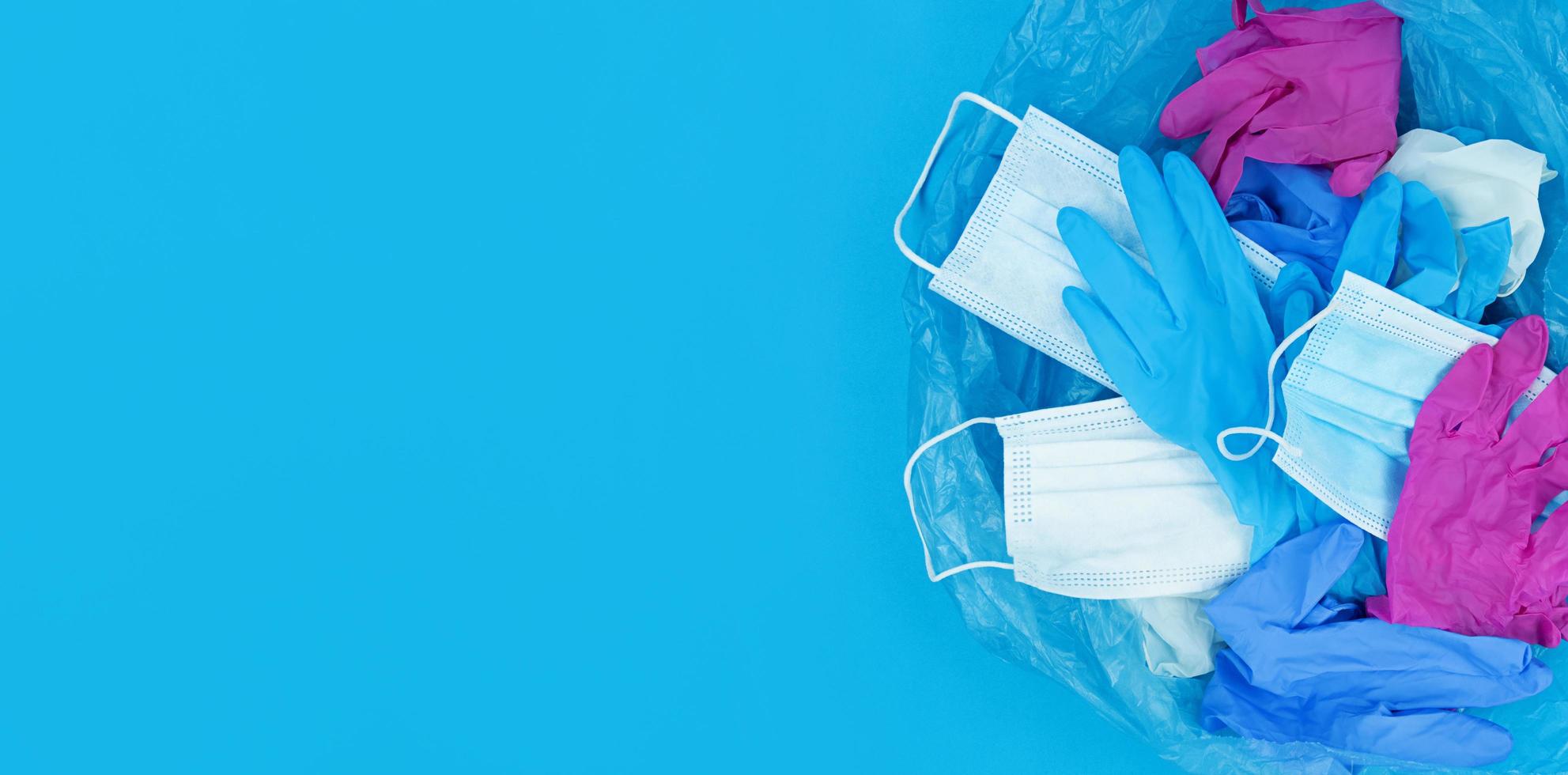 Residuos médicos del coronavirus pandémico, mascarillas y guantes de látex en una bolsa de basura sobre un fondo azul. foto