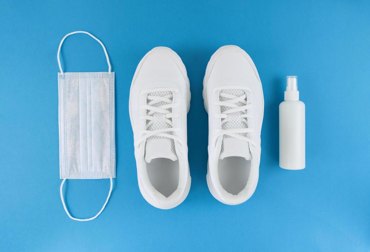 White medical mask, trainers, and hand sanitizer on a blue background, monochrome flat lay quarantine outfit photo