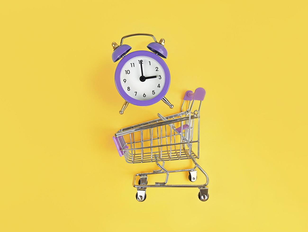 Carrito de supermercado y reloj despertador violeta sobre un fondo amarillo foto