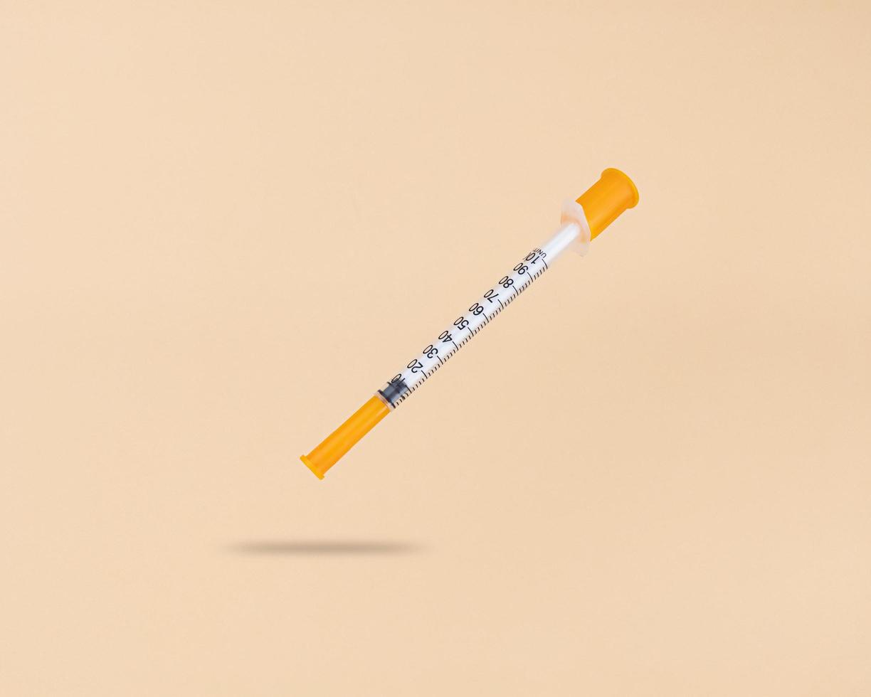 Levitation insulin syringe on a beige background with a shadow under it photo