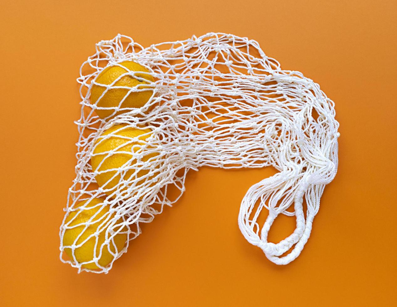 Bolsa ecológica de algodón de hilo blanco con naranjas en el interior sobre un fondo naranja, monocromo simple concepto de desperdicio cero ecología plana foto