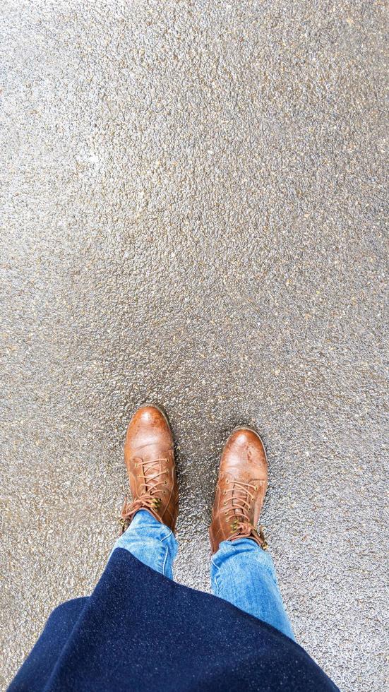 Vista superior selfie de pies de mujer en botas de otoño marrón sobre asfalto mojado después de la lluvia foto