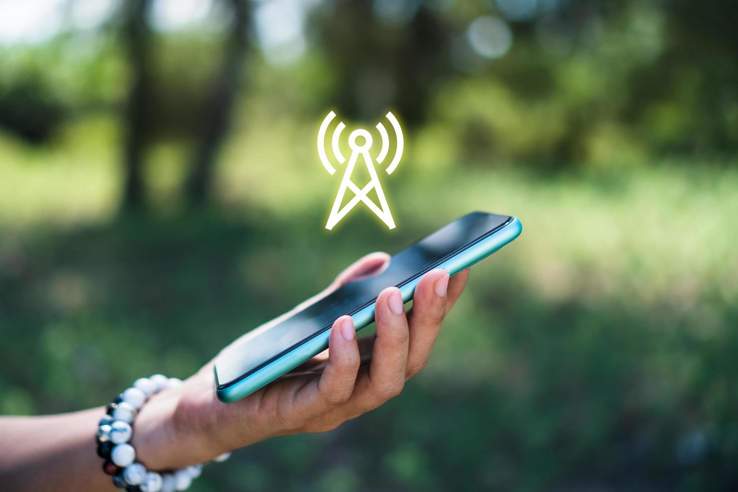 A person's hand using a smartphone with a signal wifi icon on a blurry nature background photo