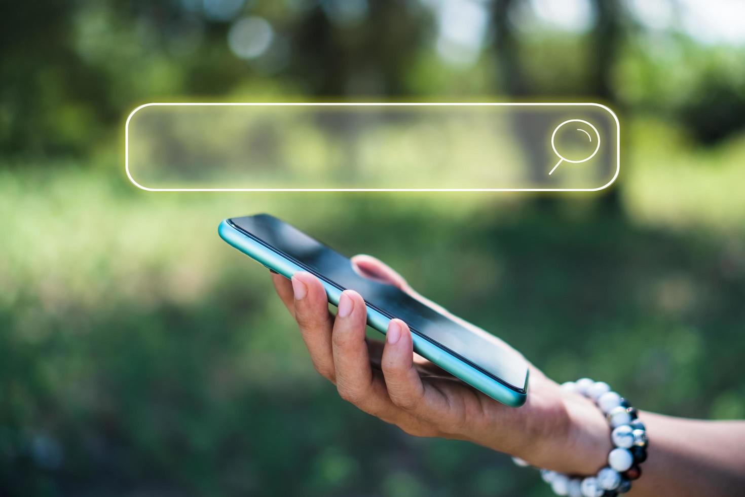 A person's hand using a smartphone with a search box icon on a blurry nature background photo