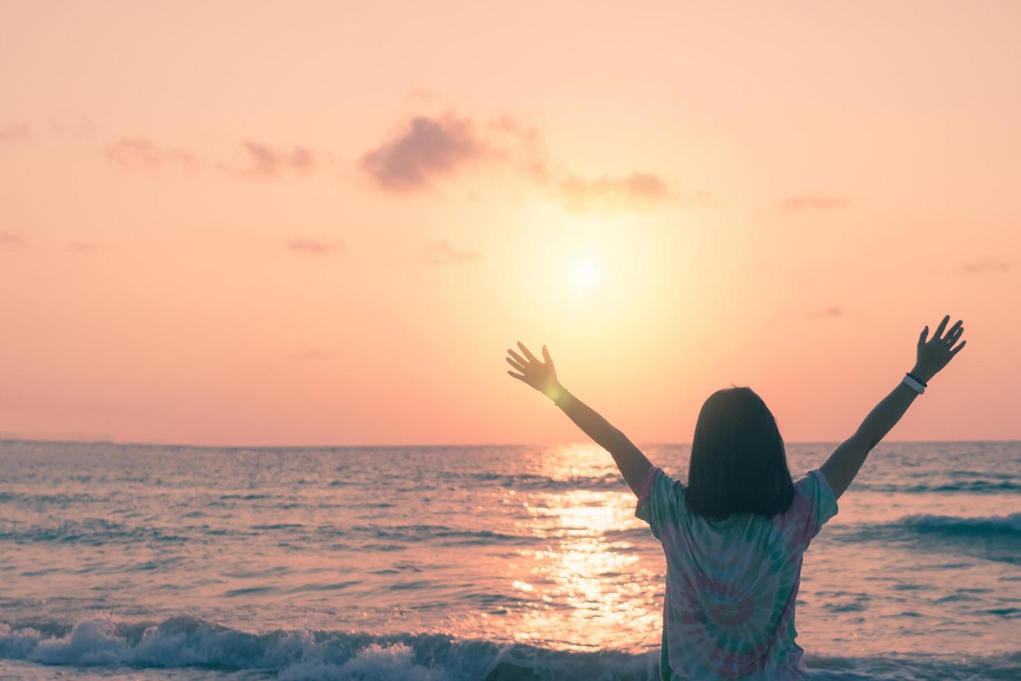 Una mujer levantando sus manos hacia el cielo en una playa durante las vacaciones de verano foto