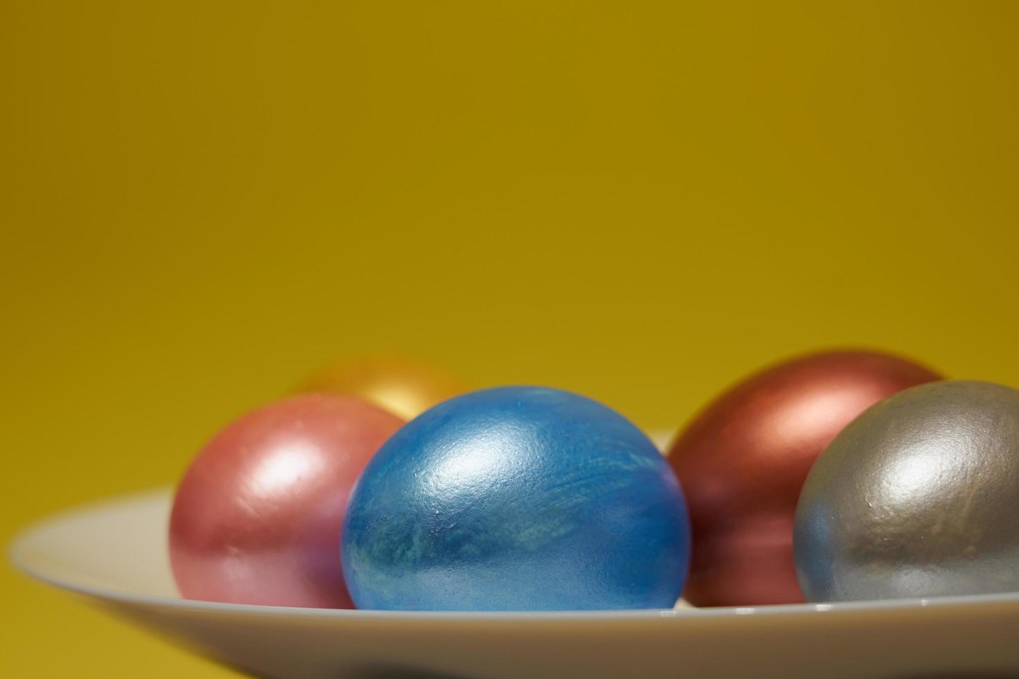 Painted eggs on a white plate with a yellow background for Easter photo
