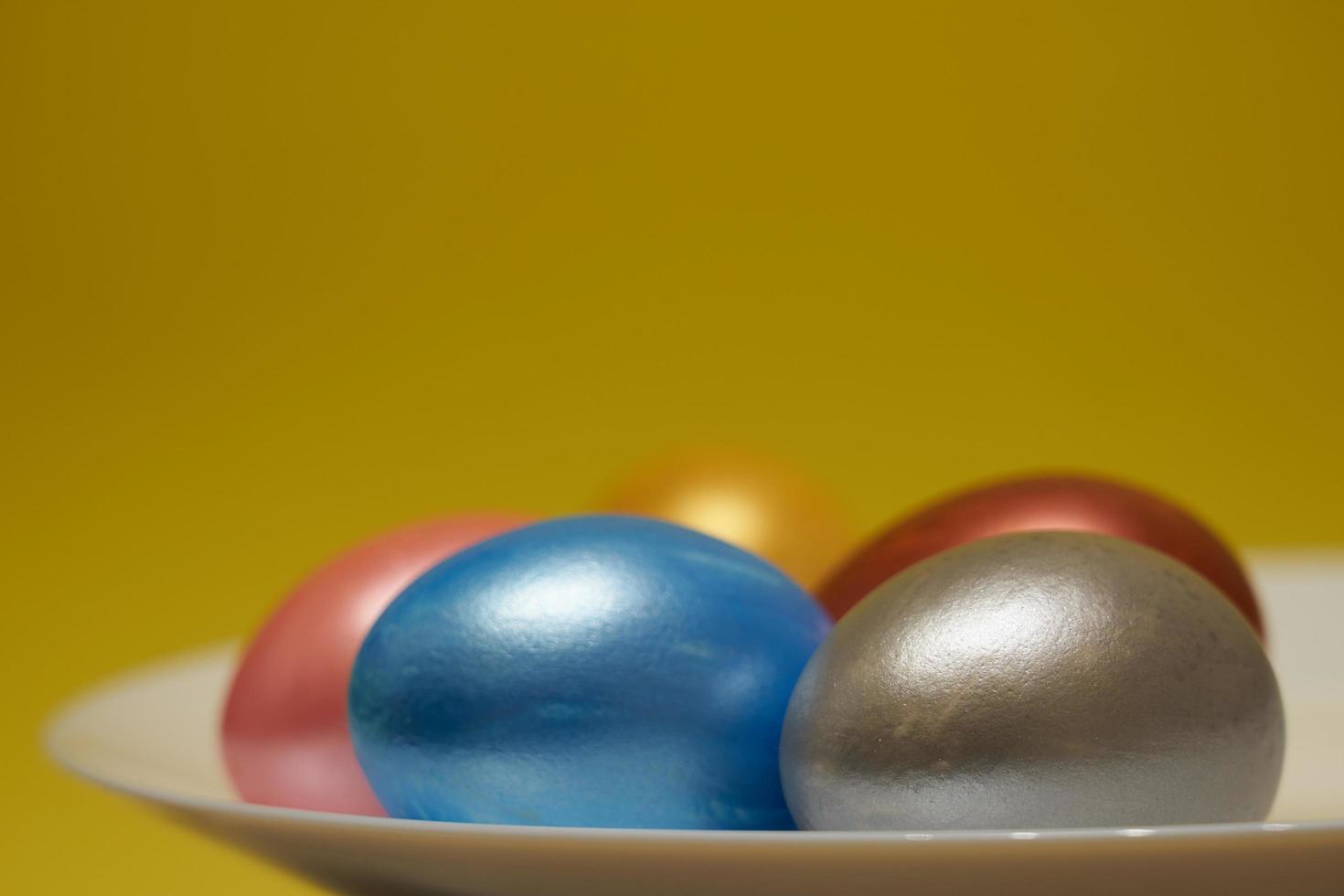 Painted eggs on a white plate with a yellow background for Easter photo