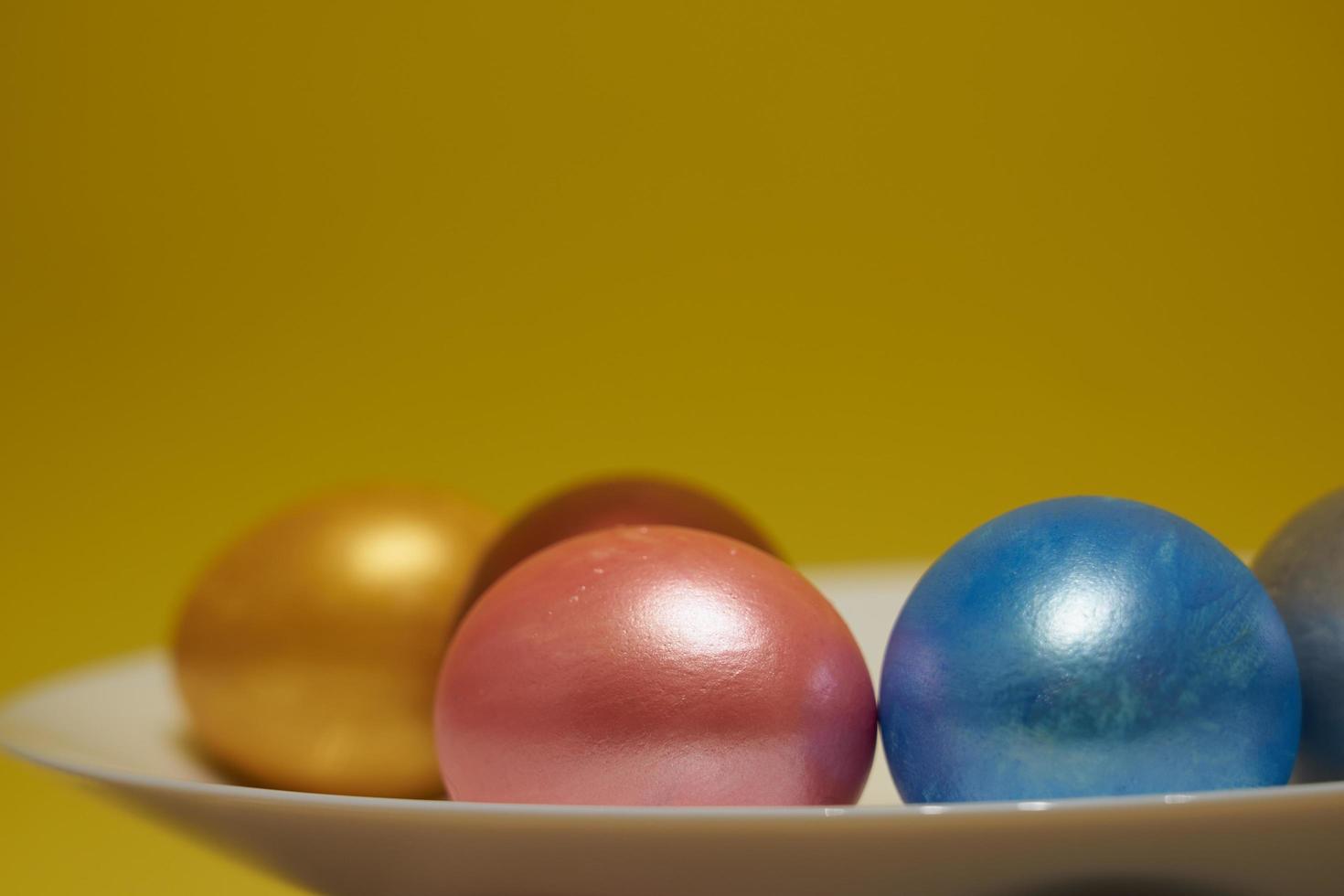 Painted eggs on a white plate with a yellow background for Easter photo