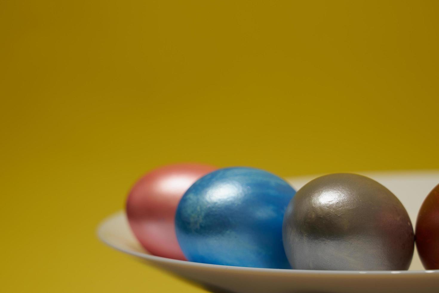 Painted eggs on a white plate with a yellow background for Easter photo