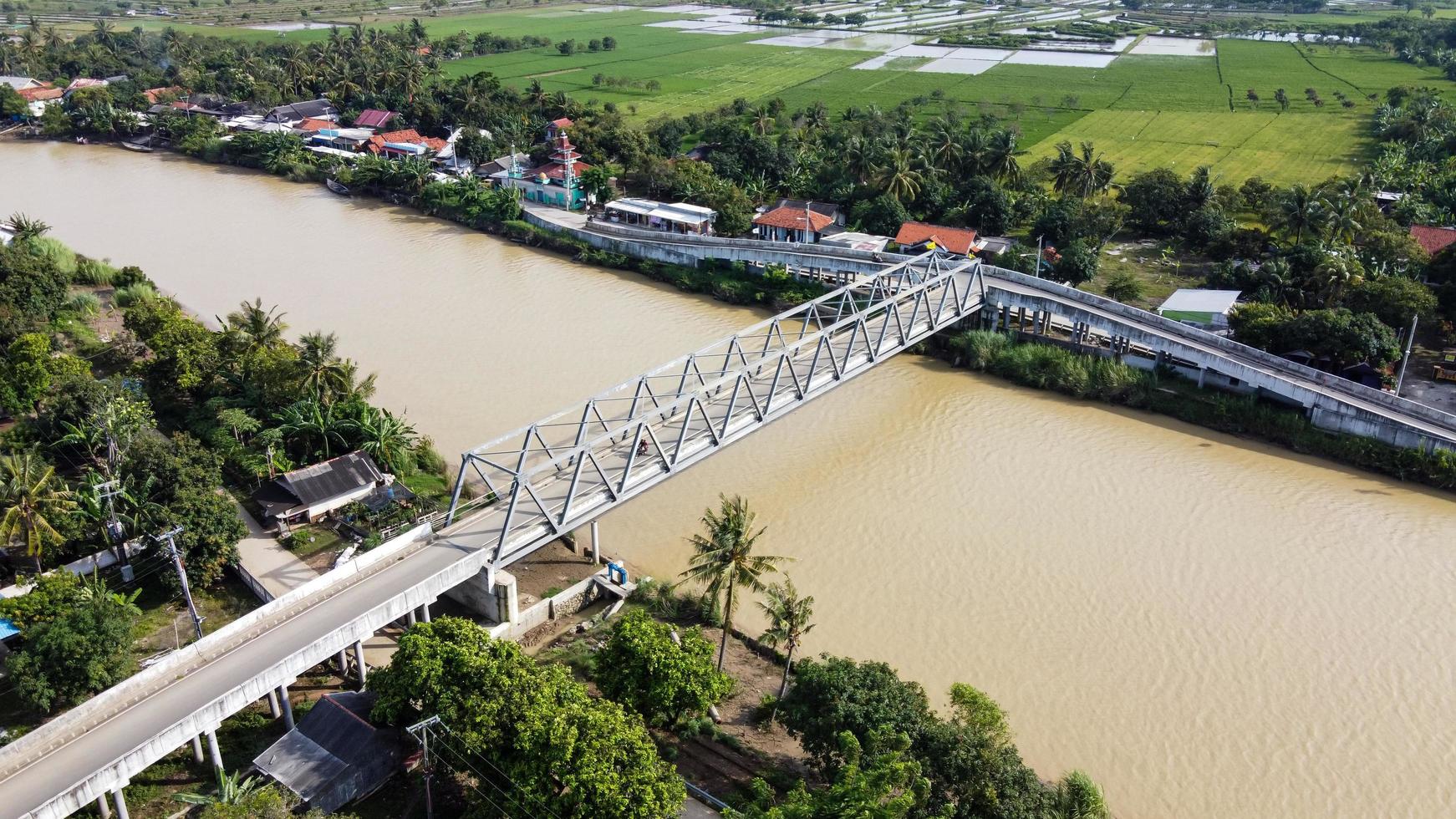 Bekasi, Indonesia 2021- Aerial drone view of a long bridge at the end of the river connecting two villages photo