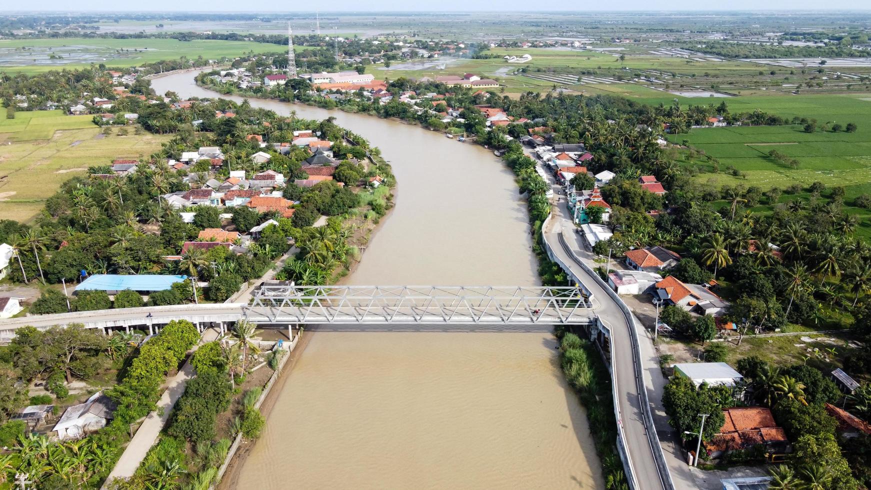 Bekasi, Indonesia 2021- Aerial drone view of a long bridge to the end of the river connecting  two villages photo