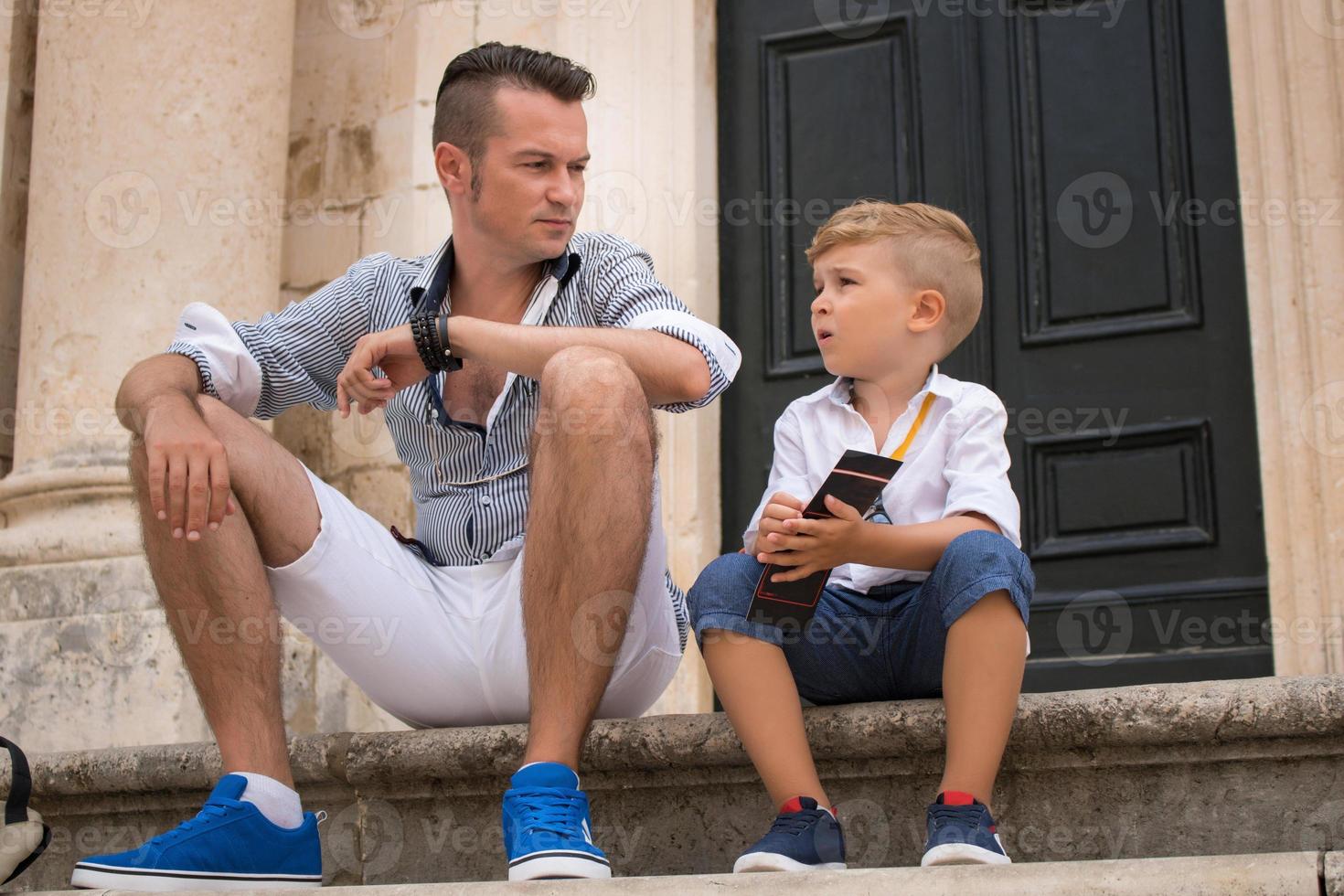 Father and son sitting on steps while relaxing in the city photo