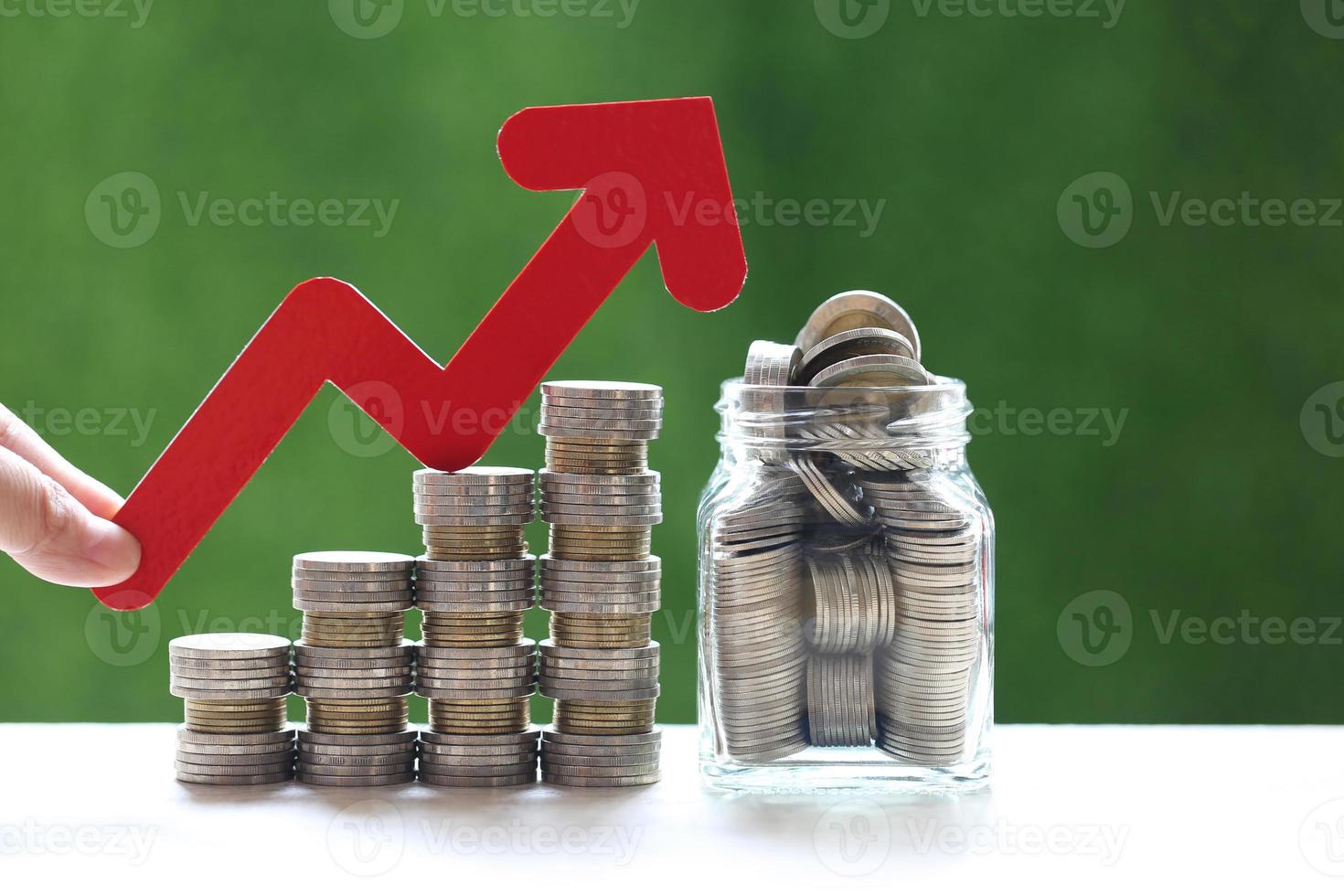 Woman's hand holding red arrow graph and stack of coins money in glass bottle photo