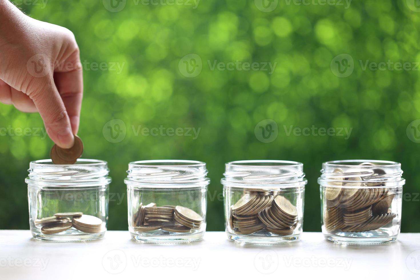 Mano de mujer poniendo una moneda en la botella de vidrio sobre fondo verde foto