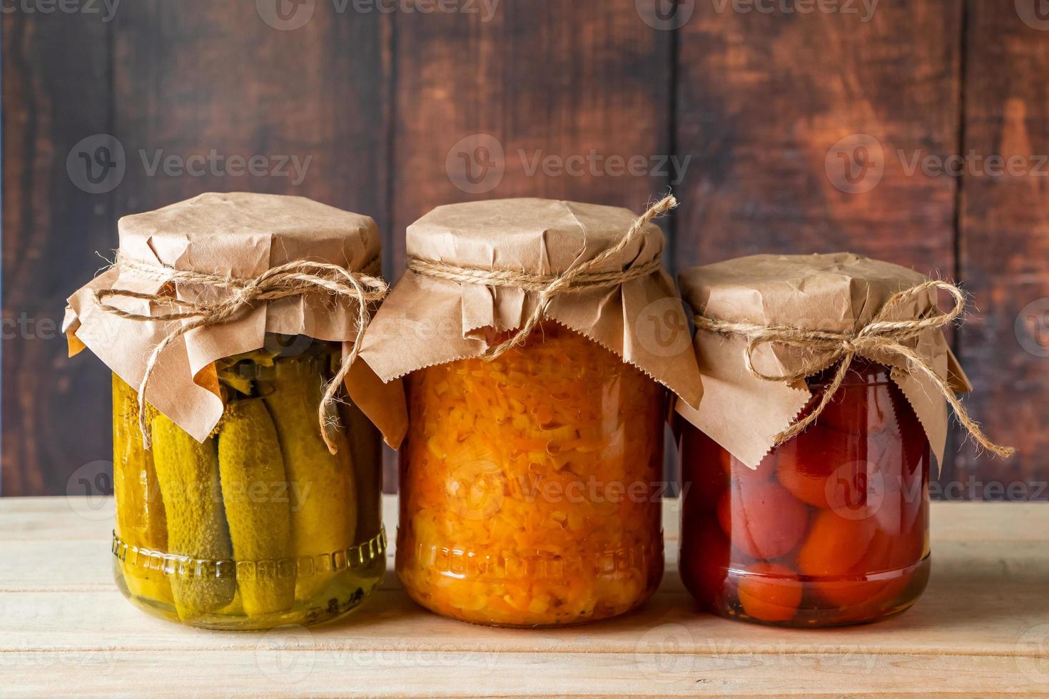 Pickled farm vegetables in glass jars on wooden background photo