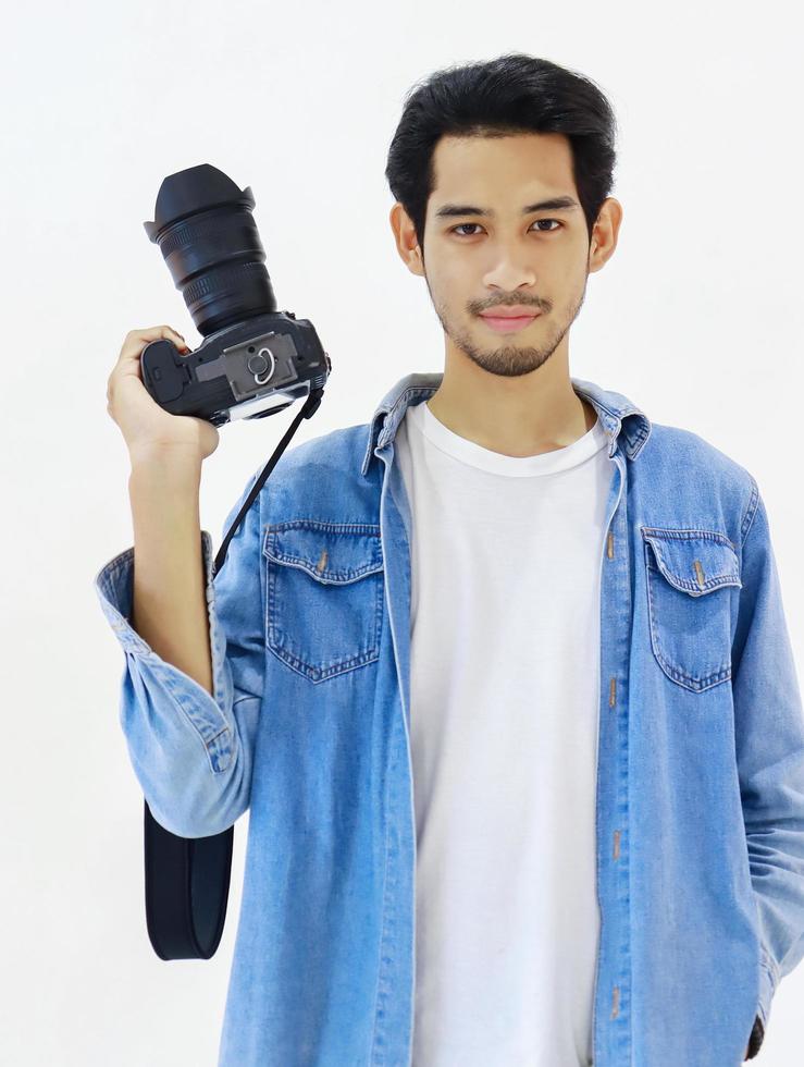 Apuesto joven fotógrafo de pie con una cámara sobre un fondo blanco. foto