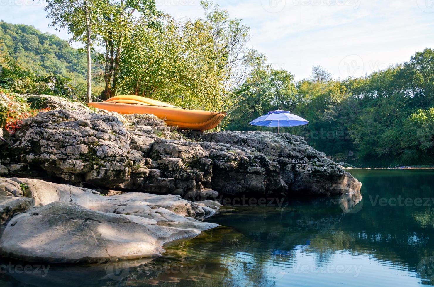 Kayak naranja y paraguas azul junto al río en el bosque foto