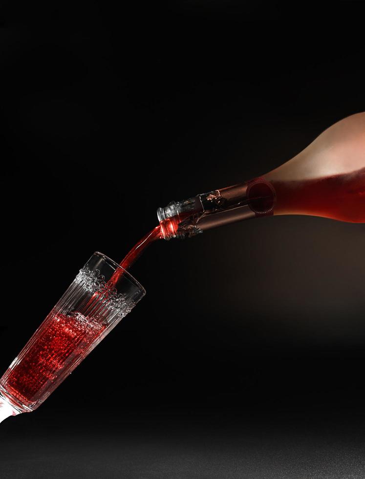 Red wine pouring into wine glass on black background photo