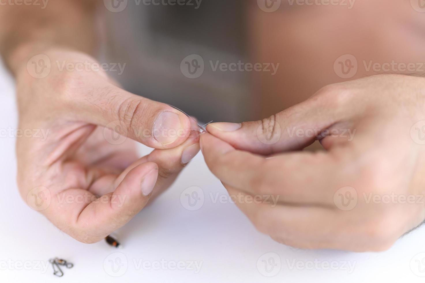 Las manos del hombre atando un hilo de pescar con una mosca en un anzuelo de pesca foto