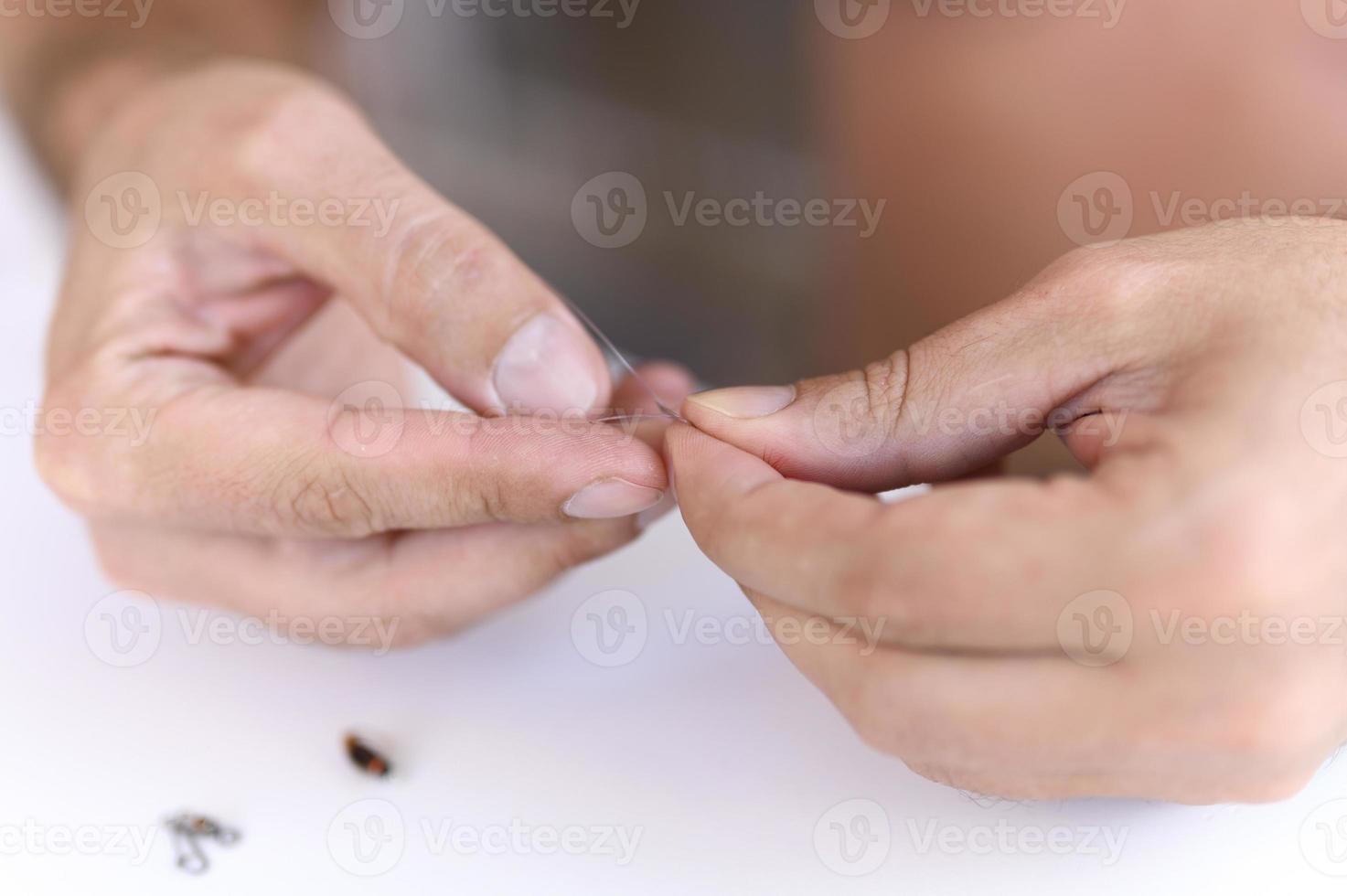 Las manos del hombre atando un hilo de pescar con una mosca en un anzuelo de pesca foto