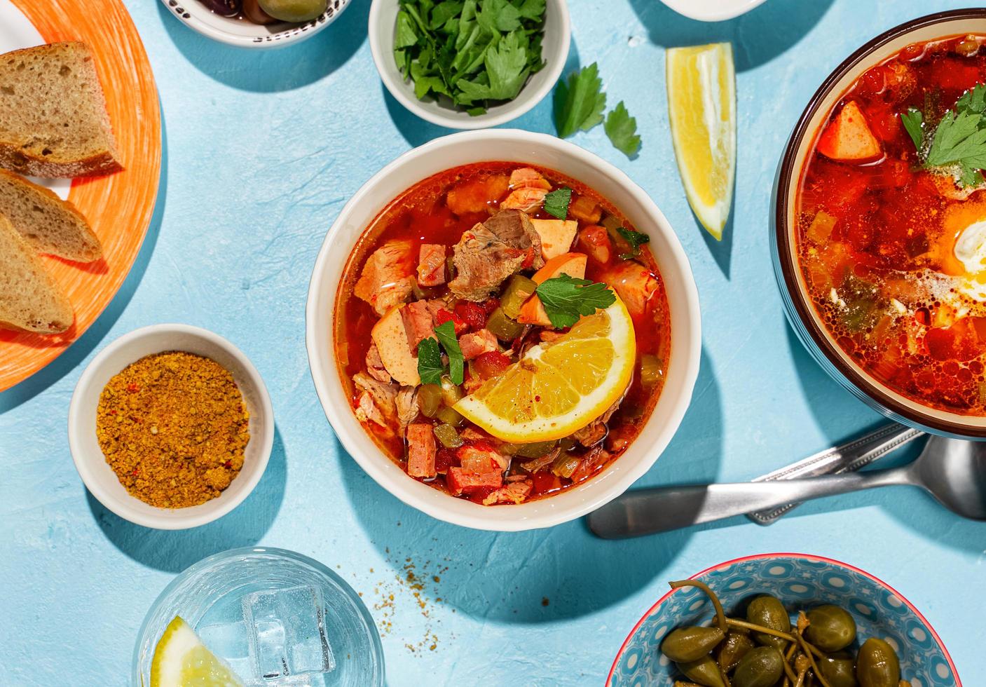 Sopa de carne solyanka casera servida con limón, aceitunas y alcaparras sobre fondo azul vibrante foto