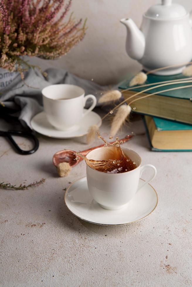 Still life with tea splashing out of tea cup, books, and flowers photo