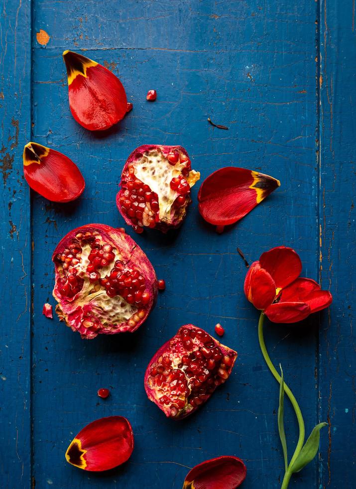 Red tulip and pomegranate with seeds on dark blue wooden background, flat layout photo