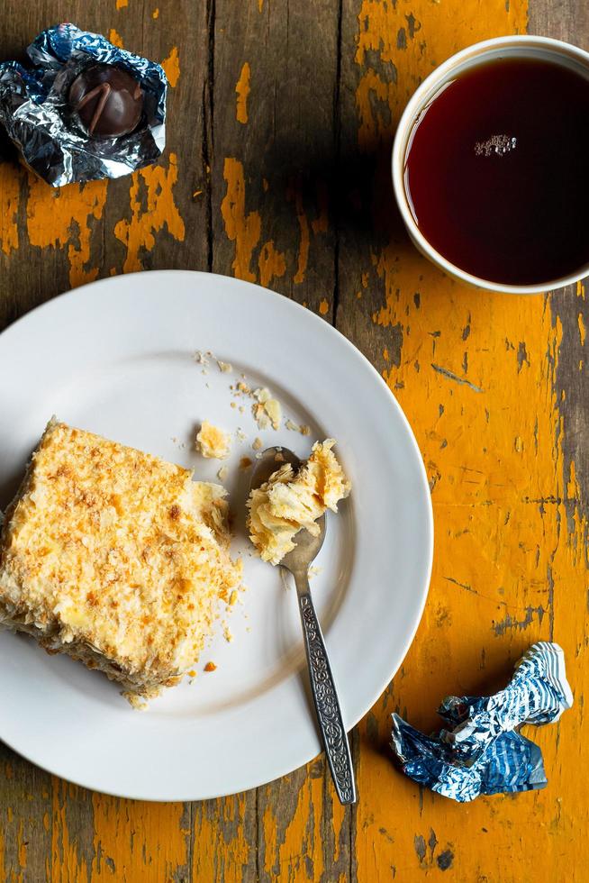 Homemade mille-feuille, puff pastry custard cream pie on white plate, chocolates, tea cup on old yellow painted wooden background photo