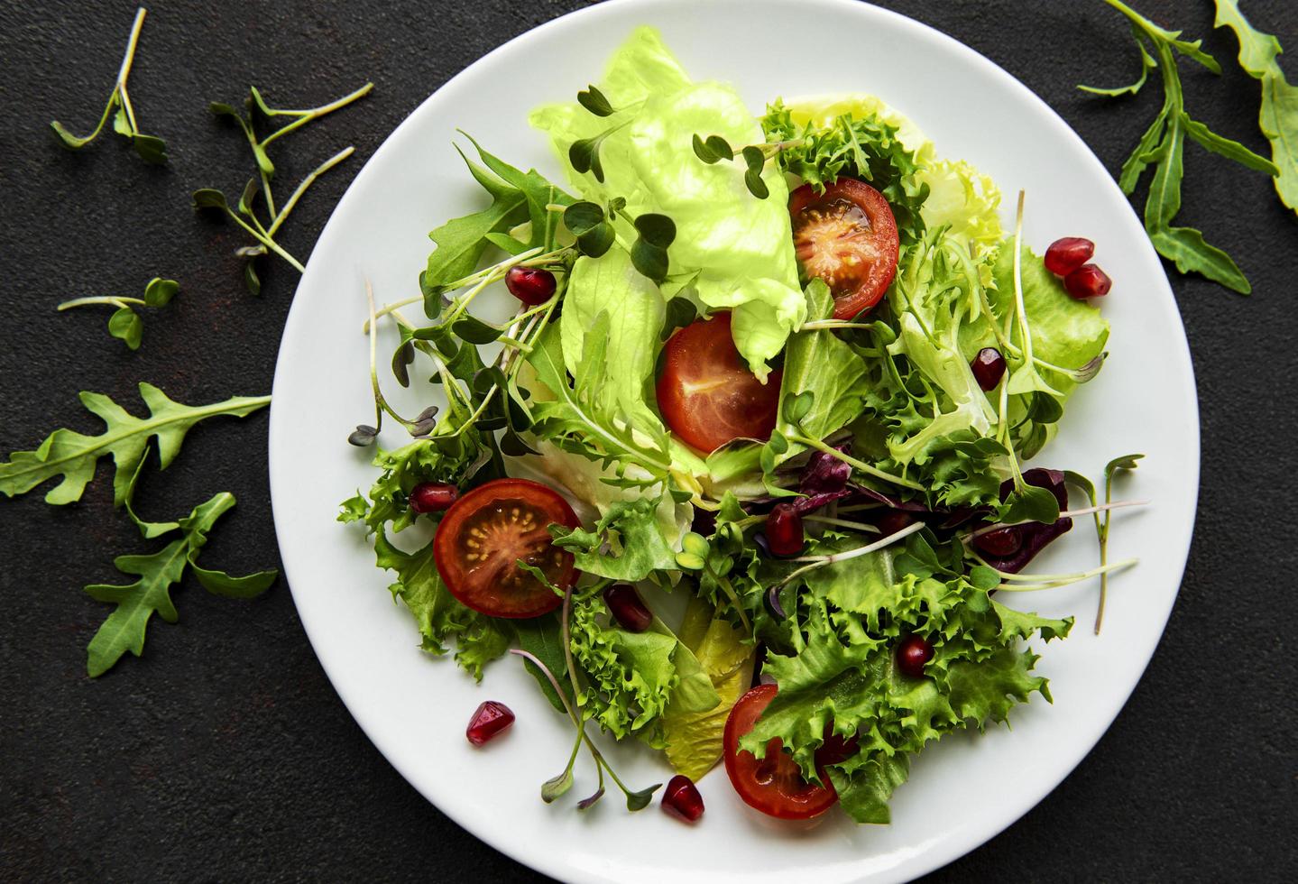 Ensaladera mixta verde fresca con tomates y microgreens sobre fondo de hormigón negro foto