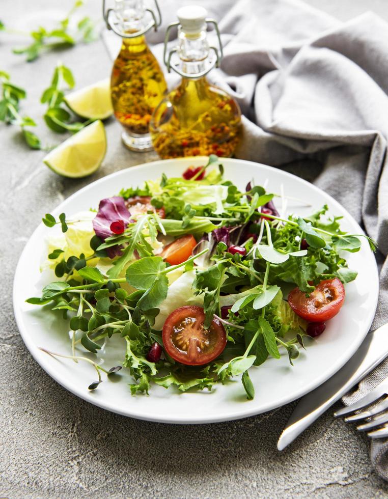 Fresh green mixed salad bowl with tomatoes and microgreens on concrete background photo