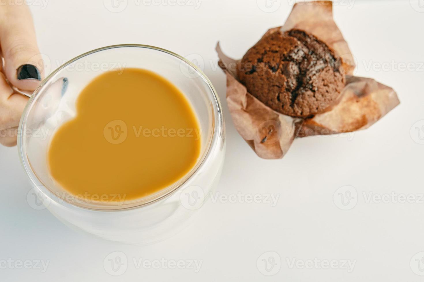 Asimiento de la mano de la mujer taza de cacao y cupcake en el cuadro blanco foto