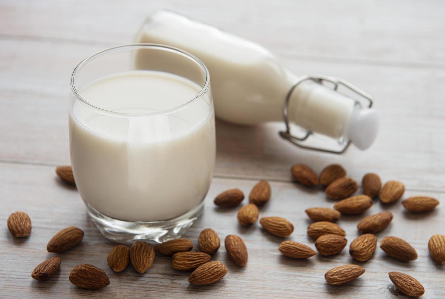 Botella de vidrio con leche de almendras y almendras en la mesa foto