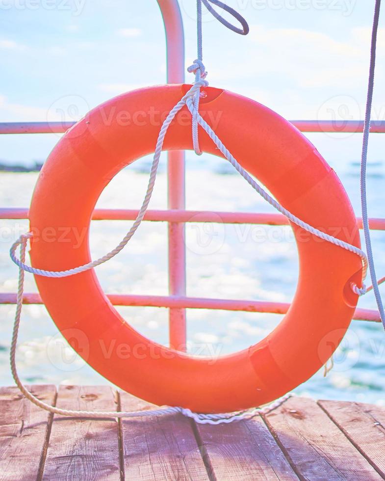 Aro salvavidas naranja con cuerda en un muelle de madera cerca del mar foto