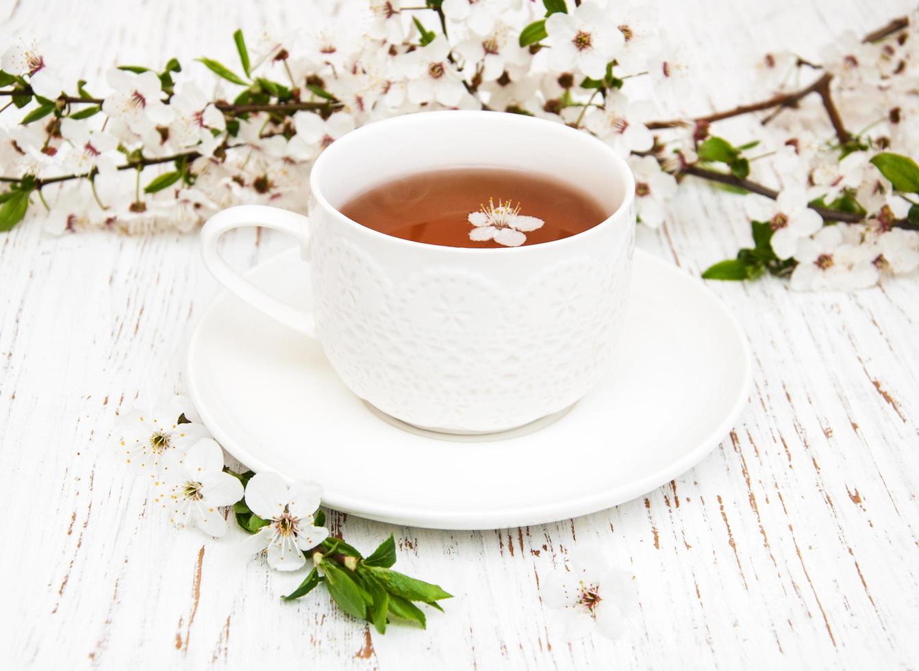 Cup of tea and spring apricot blossoms on a wooden background photo