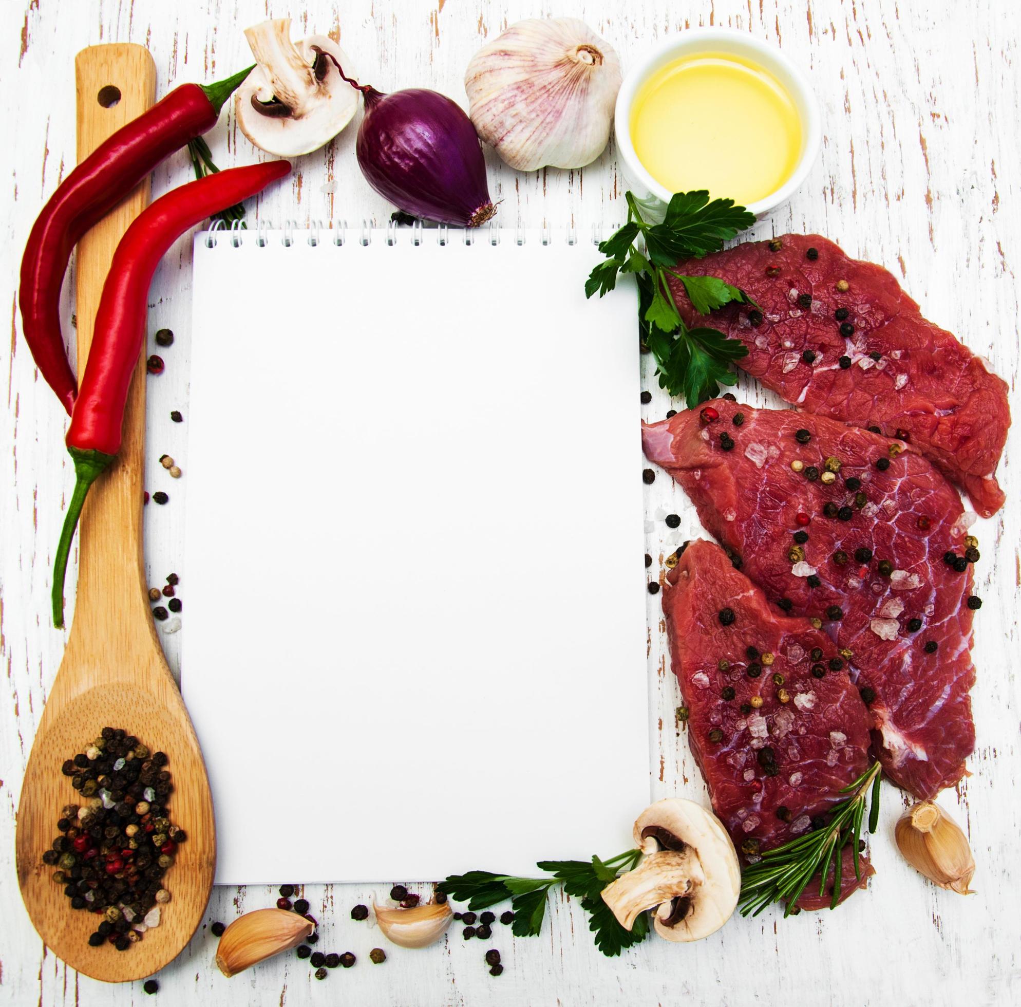 Meat steaks, a recipe book, and ingredients on an old wooden background