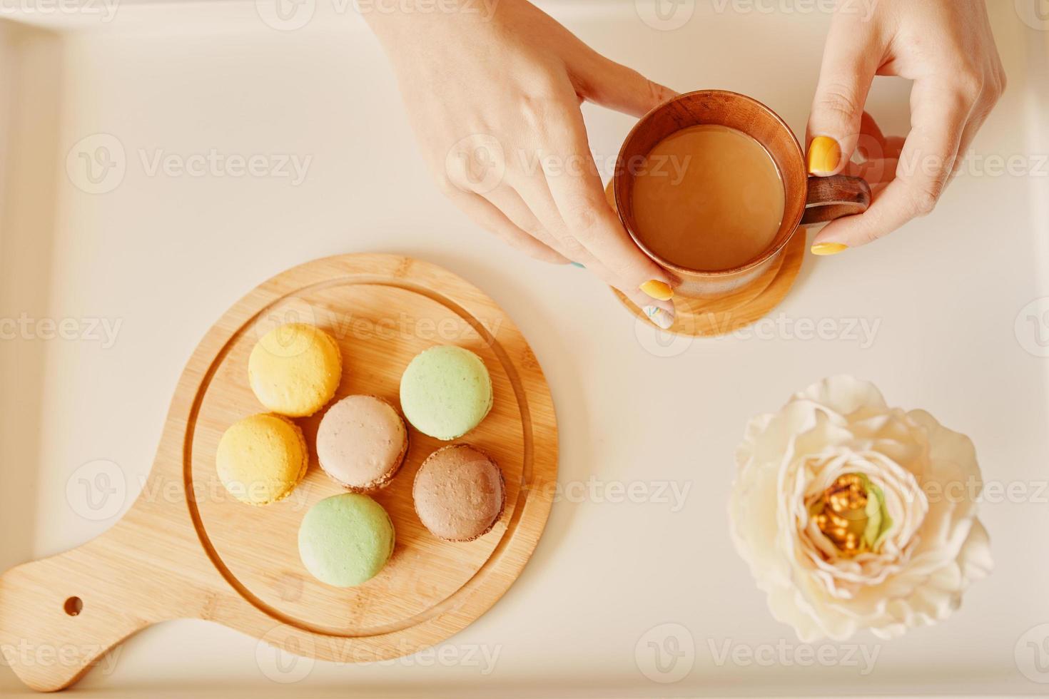 Mug of coffee in woman's hands and wooden tray with macaroons photo