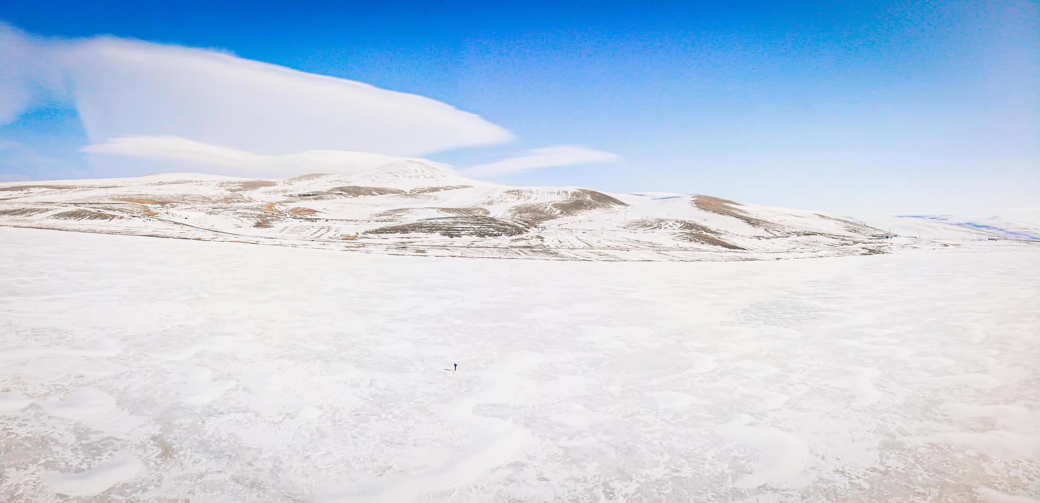 Small person stands on frozen lake surrounded with mountains photo