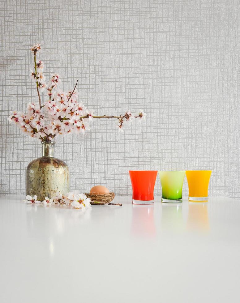 Bouquet style white kitchen table set up with yellow and green cups, blooming daisy flowers and an Easter egg photo