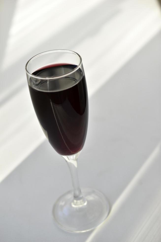 Vaso pequeño de vino tinto sobre un fondo blanco con sombras foto