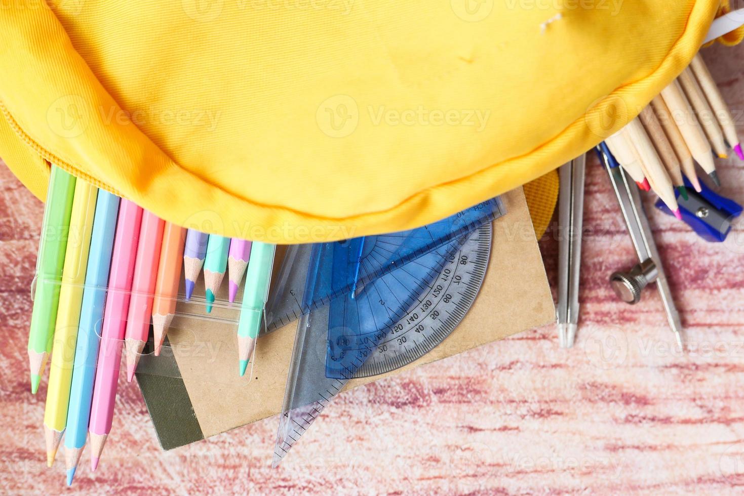 School supplies spilling out of a yellow backpack photo