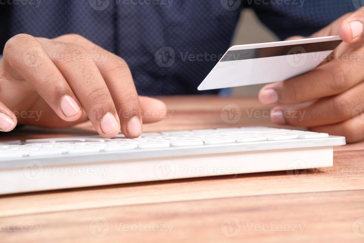 Hombre sujetando una tarjeta de crédito y escribiendo en el teclado foto
