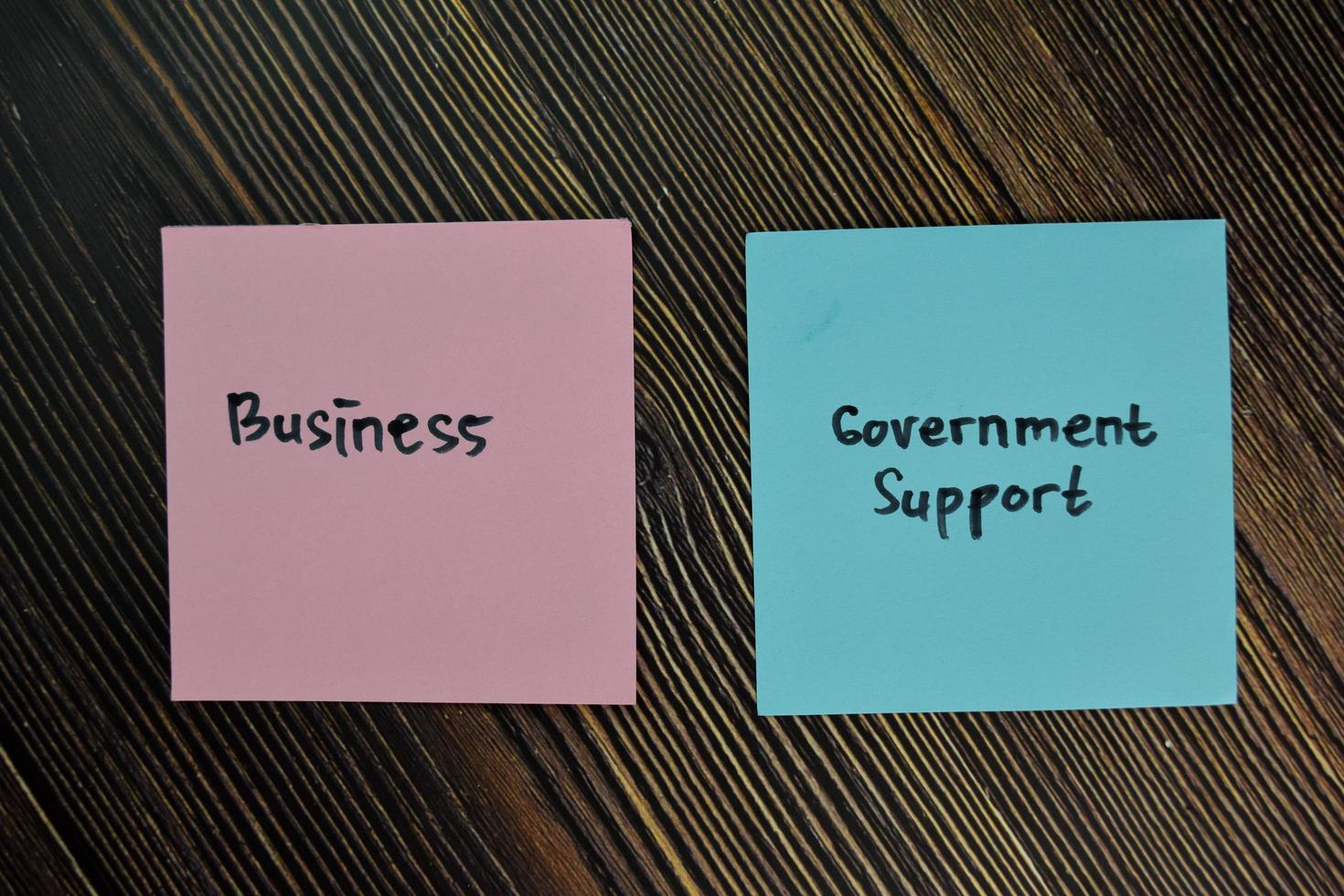 Business and government support written on sticky notes isolated on wooden table photo