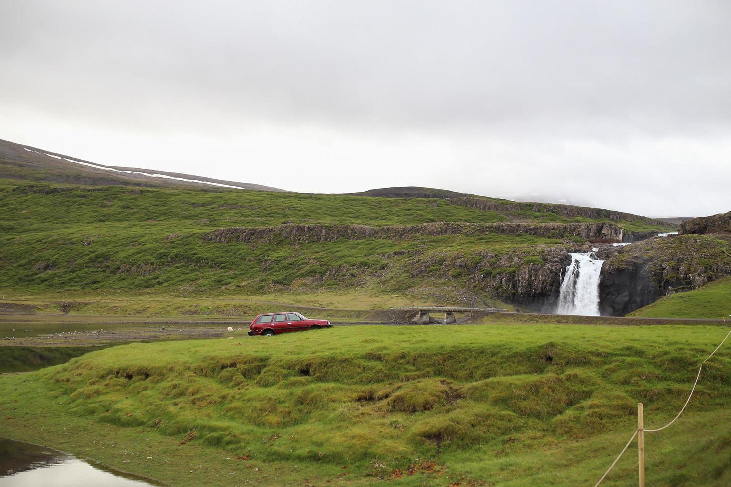 Coche rojo solitario estacionado cerca de una cascada en Islandia foto