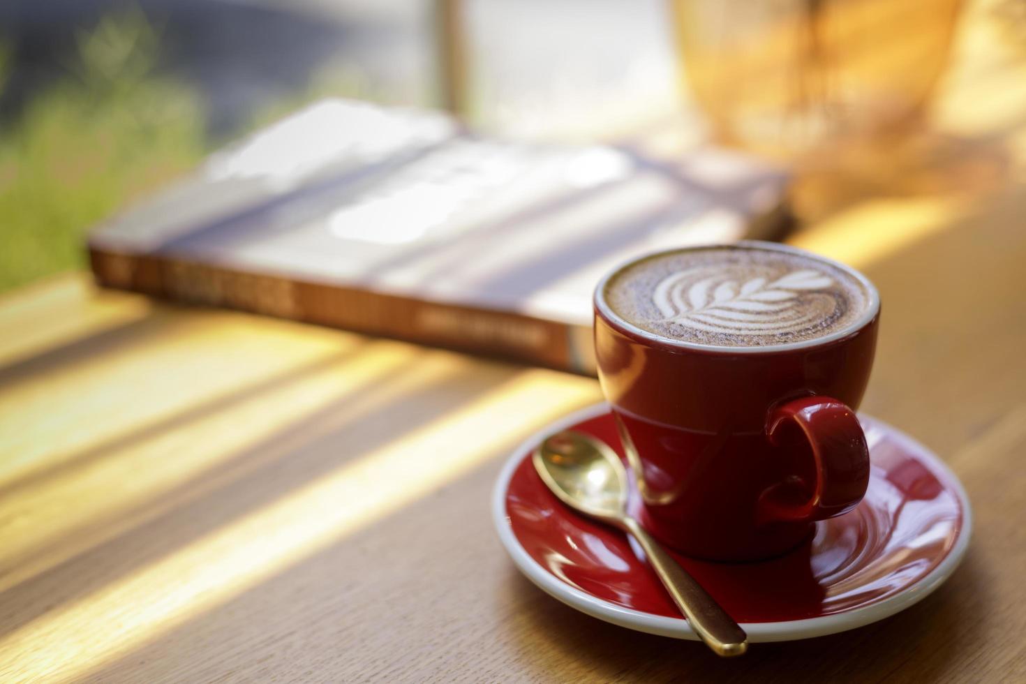 Cerca de hot art latte, café capuchino en una taza roja sobre una mesa de madera en una cafetería con un fondo borroso foto