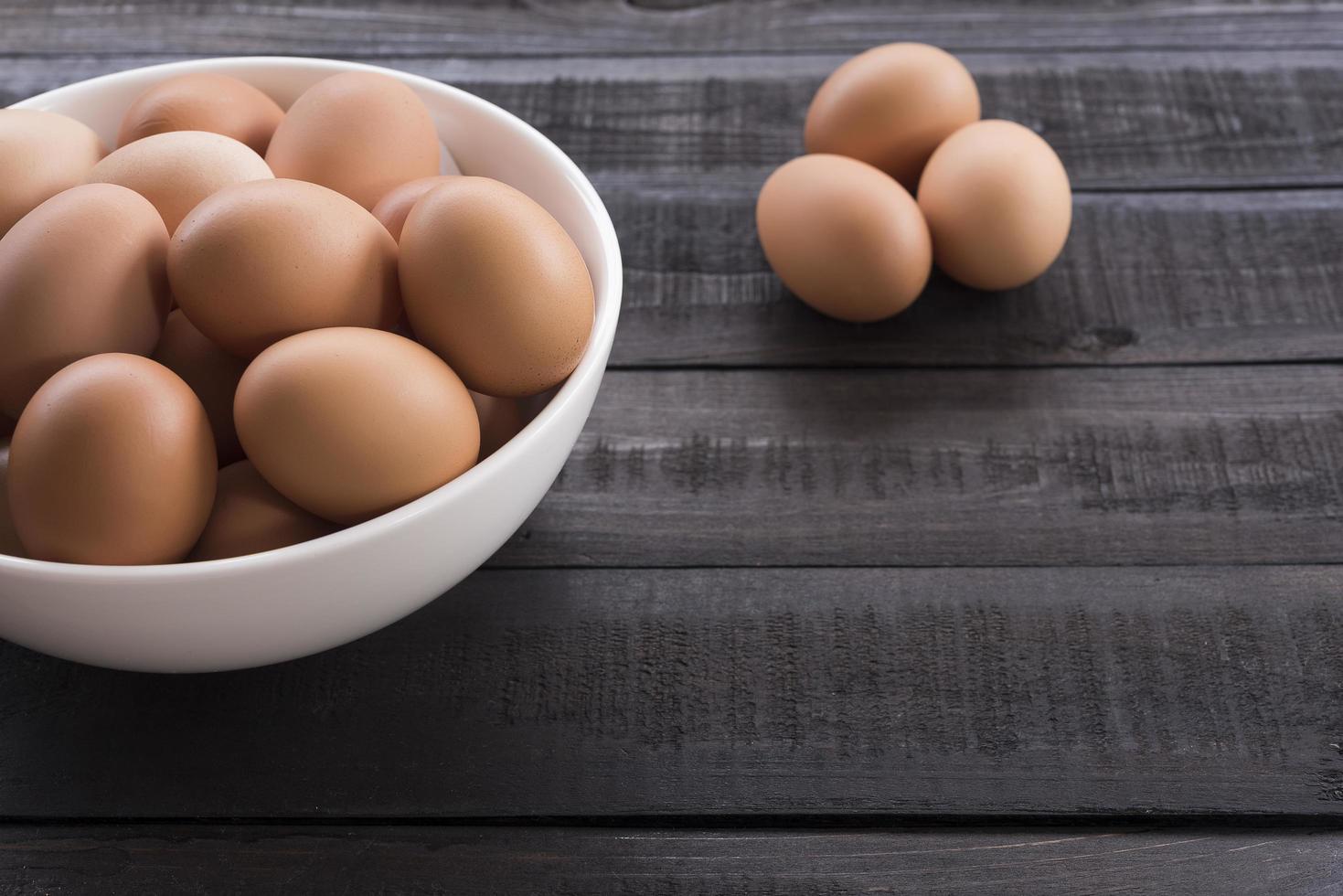 Chicken eggs in a white bowl and three chicken eggs outside on a black wooden table photo